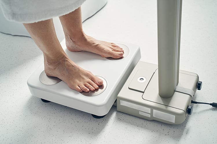 一名用户赤脚站在一台商用人体成分分析仪上，准备进行身体成分测试。